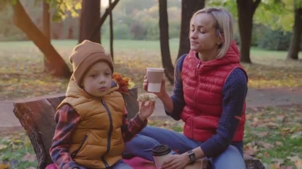 Młoda kobieta i chłopiec picia herbaty w jesienny park. Żółte liście i pić herbatę w parku. — Wideo stockowe