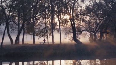 Parkta sonbahar gündoğumu bir sisli sırasında çalışan bir kadın silüeti.