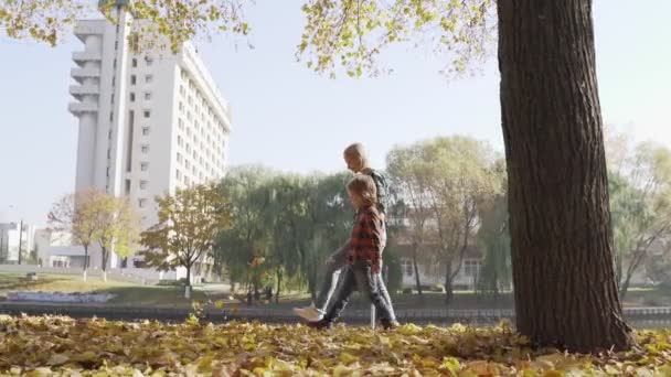 Молодая мать развлекается с сыном в осеннем парке в солнечный день — стоковое видео