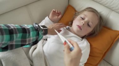 Termometreyi kapat. Anne hasta çocuğunun ateşini ölçüyor. Yüksek ateşi olan hasta çocuk yatakta yatıyor..