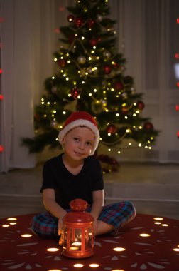 Santas kırmızı şapka oturma Noel ağacı yanında küçük çocuğa