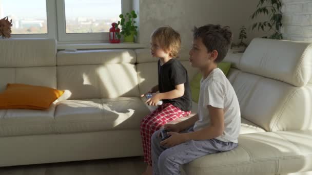 Двое детей эмоционально играют в видеоигры дома в солнечное утро — стоковое видео