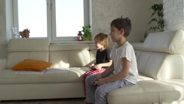 Dos niños jugando emocionalmente videojuegos en casa en la mañana soleada — Vídeos de Stock