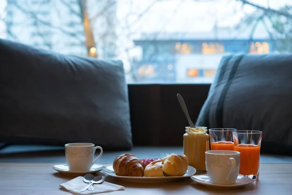 Mesa de cocina oscura con juego de desayuno. Croissant recién horneado, mantequilla de maní y café sobre tabla de madera rústica sobre fondo grunge oscuro — Foto de Stock