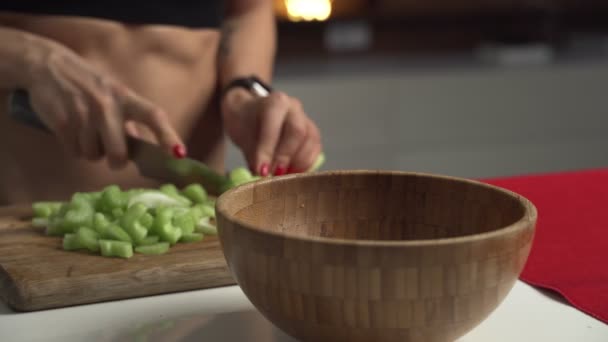 Mulher desportiva corta aipo em uma tábua de corte para cozinhar salada de legumes caseira — Vídeo de Stock