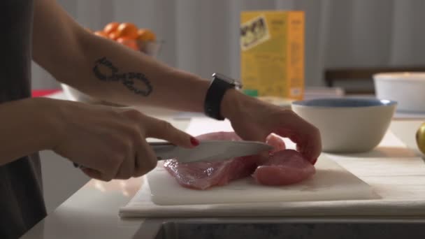 Close-up vrouw snijdt kip met een mes op een bord. Vrouwelijke handen chef-kok snijden rauw vlees kipfilet. — Stockvideo