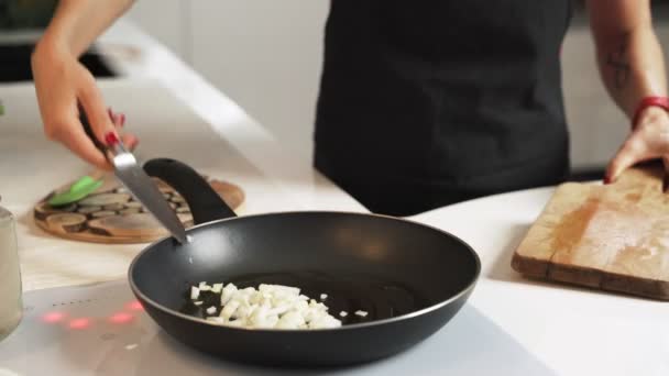 Mujer corta lentamente cebolla sobre tabla de cortar de madera en la cocina — Vídeo de stock