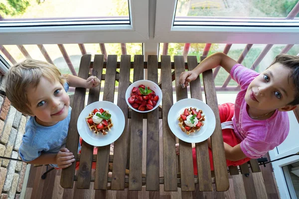 Dos niños comen para el desayuno gofres vieneses con helado y fresas — Foto de Stock