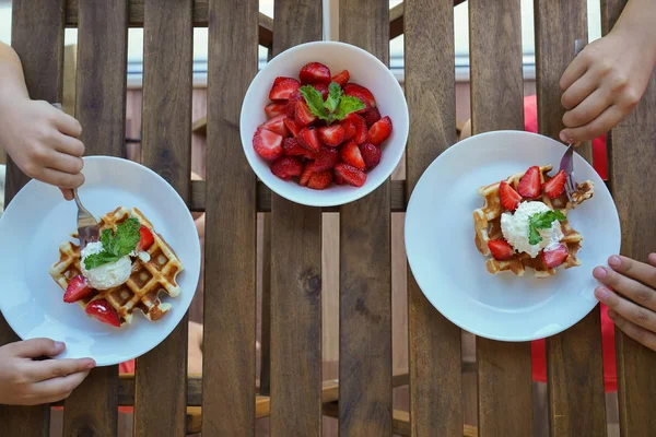 Deux garçons mangent pour le petit déjeuner gaufres viennoises avec de la crème glacée et des fraises. Vue du dessus . — Photo