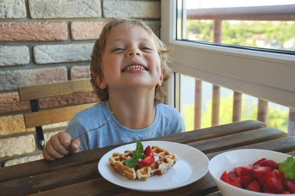 Happy 5 year old caucasian boy eat for Breakfast Viennese waffles with ice cream and strawberries — Stock Photo, Image