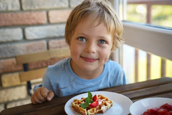 Happy 5 year old caucasian boy eat for Breakfast Viennese waffles with ice cream and strawberries — Stock Photo, Image