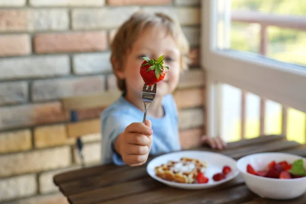 Feliz niño caucásico de 5 años comer para el desayuno gofres vieneses con helado y fresas — Foto de Stock