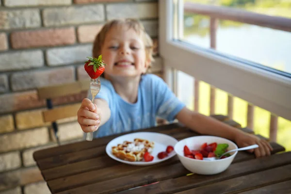 Feliz niño caucásico de 5 años comer para el desayuno gofres vieneses con helado y fresas — Foto de Stock