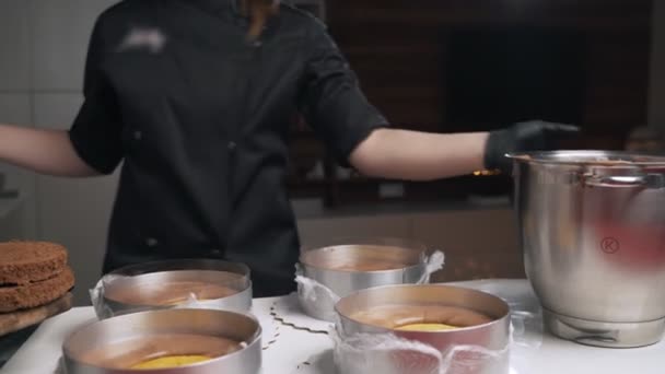 Vrouw banketbakker in zwart uniform bereiden crème voor chocolademousse taart. Fase koken mousse taart — Stockvideo