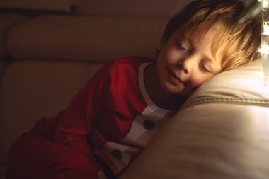 Güzel çocuk Noel gece kanepede uyuyor. Noel ağacının altında uyuyan çocuk