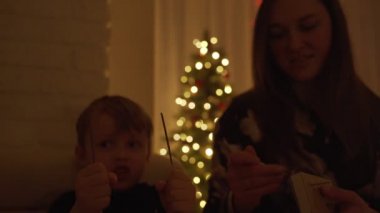 Çocuk tutan bir maytap ve gülüyor. Havai fişekleri. Havai fişekleri onun elinde. Yeni yıl ruh. Noel ağacı. Işıklar. Yakışıklı çocuk. Çocuk.