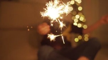 Çocuk tutan bir maytap ve gülüyor. Havai fişekleri. Havai fişekleri onun elinde. Yeni yıl ruh. Noel ağacı. Işıklar. Yakışıklı çocuk. Çocuk