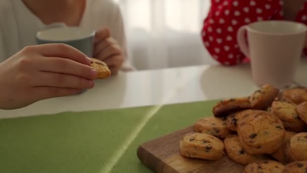 Um menino caucasiano bonito adorável está comendo biscoito ao lado de sua jovem mãe com cabelo loiro . — Vídeo de Stock