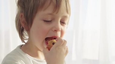 Modern mutfakta kahvaltı var. Çocuk süt ile kurabiye ye. Beyaz masa mutfak. Tablo üzerinde gri kase.