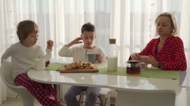 İki erkek modern mutfakta kahvaltı. Çocuk süt ile kurabiye ye. Beyaz masa mutfak. Anne ve iki oğlu kahvaltı edelim. Süt ile tanımlama.