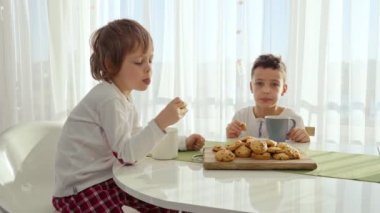 İki erkek modern mutfakta kahvaltı. Çocuk süt ile kurabiye ye. Beyaz masa mutfak. Anne ve iki oğlu kahvaltı edelim. Süt ile tanımlama.
