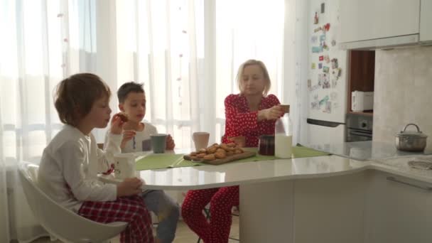 Dva chlapci snídat v moderní kuchyni. Chlapce jíst cookie s mlékem. Bílá tabulka v kuchyni. Matka a dva synové mají snídani. Soubory cookie s mlékem. — Stock video