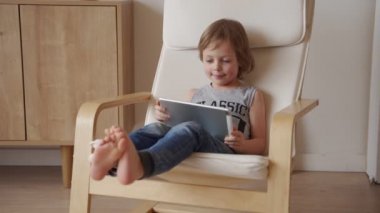 Sevimli beyaz çocuğun 5 yıllık otur armchar ve kullanım tablet ışık odasında