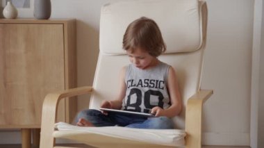 Sevimli beyaz çocuğun 5 yıllık otur armchar ve kullanım tablet ışık odasında
