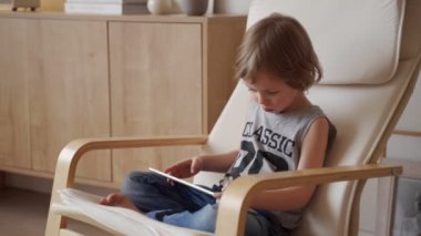 Sevimli beyaz çocuğun 5 yıllık otur armchar ve kullanım tablet ışık odasında