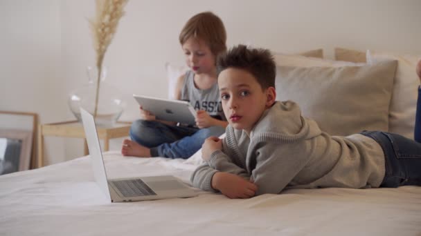 Мальчики в постели родителей по утрам с ноутбуком и планшетом. Братья играют в компьютерные игры. Братья и сестры и гаджеты . — стоковое видео