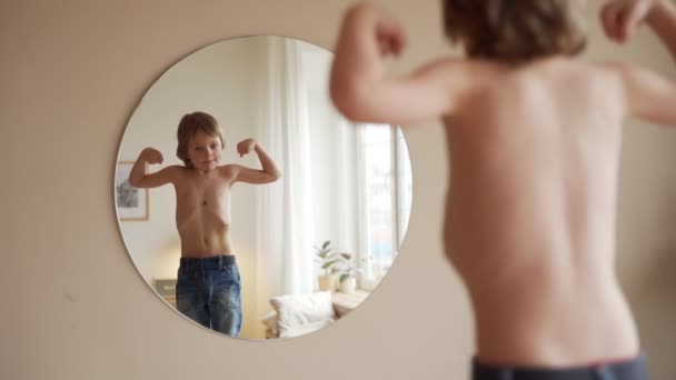 Niño confiado mirando sus músculos en el espejo imaginando que él es súper héroe — Vídeo de stock