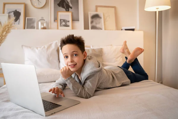 Bir dizüstü bilgisayar kitap ve kameraya görünüyor büyük bir yatak üzerinde oturan küçük bir çocuk.