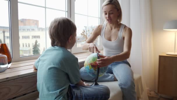 Привлекательная мать кавказской национальности использует глобус, чтобы показать своему маленькому сыну страны мира . — стоковое видео