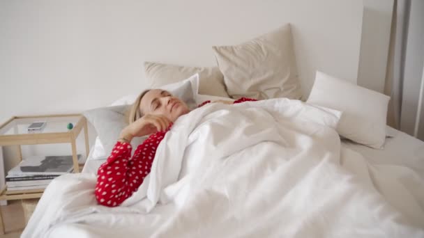 Buenos días. Joven encantadora juguetona con el pelo de jengibre acostado en la cama bajo cubierta blanca, estirando, levantando brazos, teniendo grandes planes para el día. Linda chica descansando en su dormitorio, sonriendo felizmente — Vídeo de stock