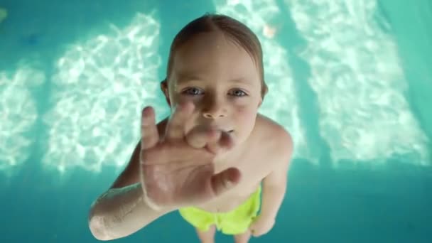 6 χρονών αγόρι που πέφτει στην πισίνα με μπλε νερό. Οι σταγόνες πετούν σε διαφορετικές κατευθύνσεις. Αργή κίνηση — Αρχείο Βίντεο