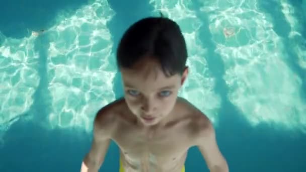 Дев'ятирічний хлопчик падає в басейн з блакитною водою. Чіпси літають в різних напрямках. Повільний рух — стокове відео