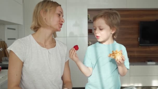 Moeder en zoon eten aardbeien in de keuken. Gelukkig familieconcept. — Stockvideo