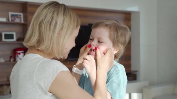 Madres mano amorosamente sosteniendo la barbilla de pequeño niño guapo sonriente mostrando sus dientes infantiles divertidos blancos en casa. Concepto de relaciones familiares felices, salud y problemas dentales — Vídeo de stock