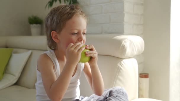6 летний мальчик ест зеленое яблоко и попробуйте вырвать молочные зубы — стоковое видео
