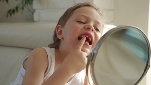 Un niño pequeño con el pelo rubio con espejo abriendo la boca para mostrar donde perdió uno de sus dientes de bebé — Vídeo de stock