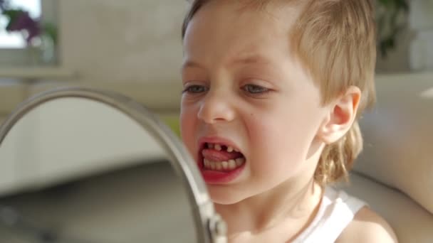 Egy kis fiú, szőke haja tükörképe a száját megmutatni, ahol elvesztette az egyik Babys fogak — Stock videók