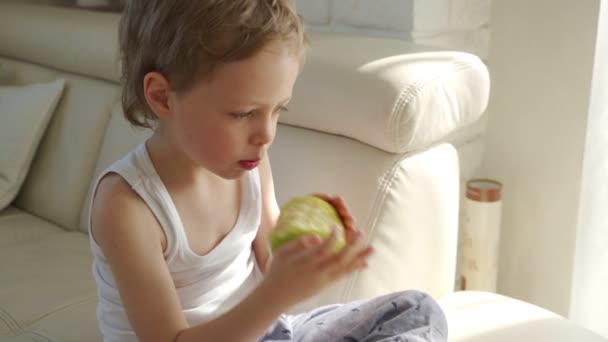 6 летний мальчик ест зеленое яблоко и попробуйте вырвать молочные зубы — стоковое видео