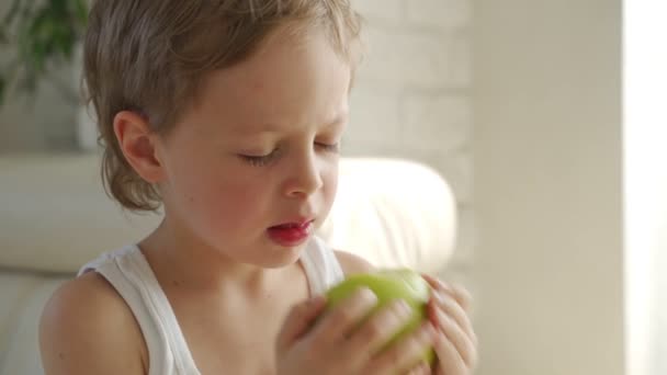 6 year old boy eating green apple and try pull out baby teeth — Stock Video