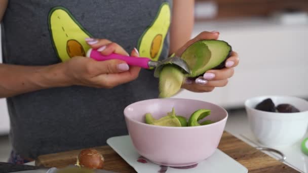 Une femme enlève la moitié de l'avocat avec une cuillère et la coupe en tranches. Femme coupe et tranche un avocat pour faire guacamole côté table. Alimentation végétarienne saine . — Video