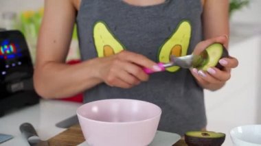 Bir kadın bir kaşık ile avokado yarısını kaldırır ve dilimleri içine keser. Kadın masa kenarı guacamole yapmak için bir avokado dilimleri ve dilim. Sağlıklı vejetaryen gıda.