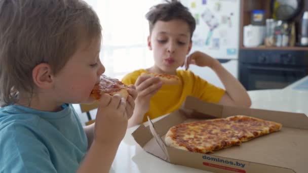 Twee kleine Kaukasische jongens eten pizza thuis. Dag licht — Stockvideo