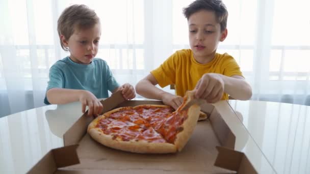 Dva malí kavkazští hoši jedí pizzu doma. Denní světlo