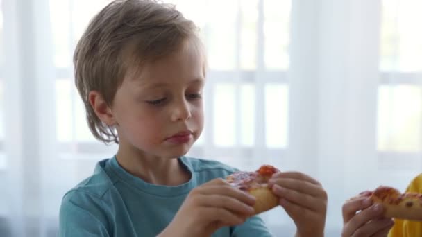 Due ragazzini caucasici che mangiano pizza a casa. Luce del giorno — Video Stock