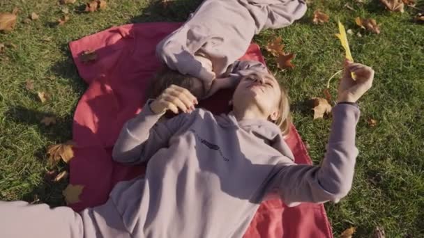 Moeder en zoon liggen op de grond en kijken door herfstbladeren naar de hemel. Mooie jongen met zijn moeder ligt op de grond in het lichte herfstbos. Moeder en haar — Stockvideo
