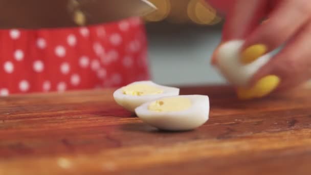 Wanita dalam irisan apron telur puyuh setengah untuk persiapan salad dengan pisau memotong papan kayu di atas meja dapur kayu. Close-up — Stok Video